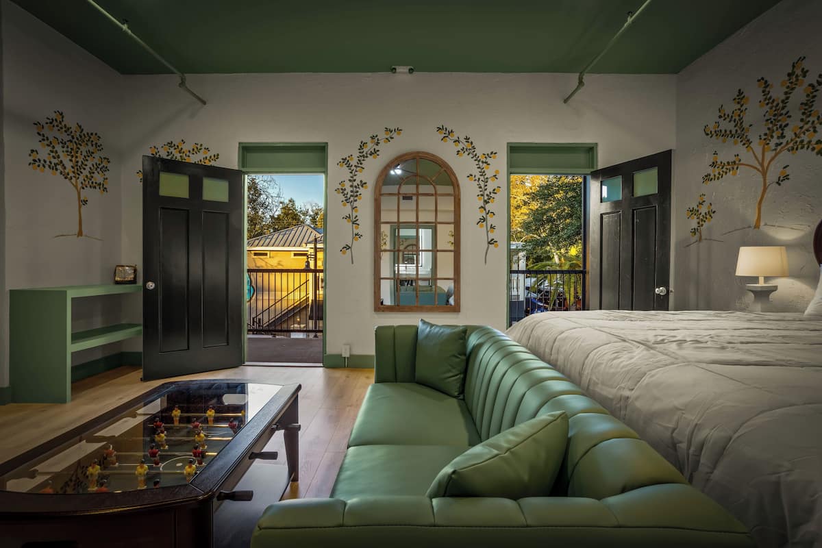 Ein Zimmer mit einem grünen Sofa, einem Bett, einem Kicker und Blick auf ein Gebäude.