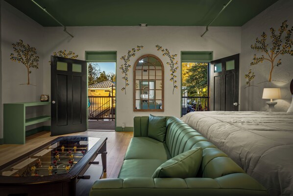 Una habitación con sofá verde, cama, mesa de futbolín y vista a un edificio.