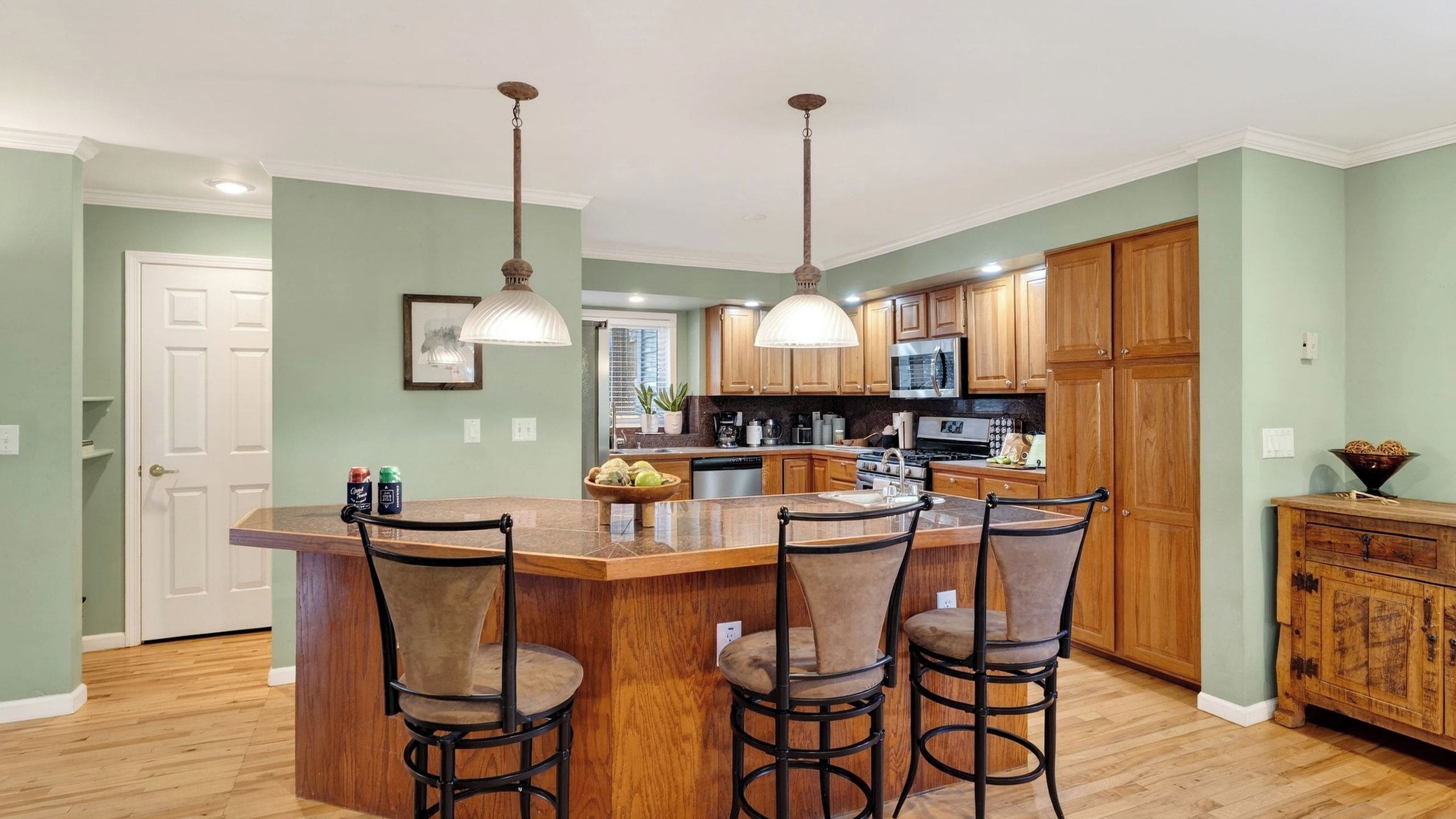 A kitchen with a central island, wooden cabinets, and pendant lighting.