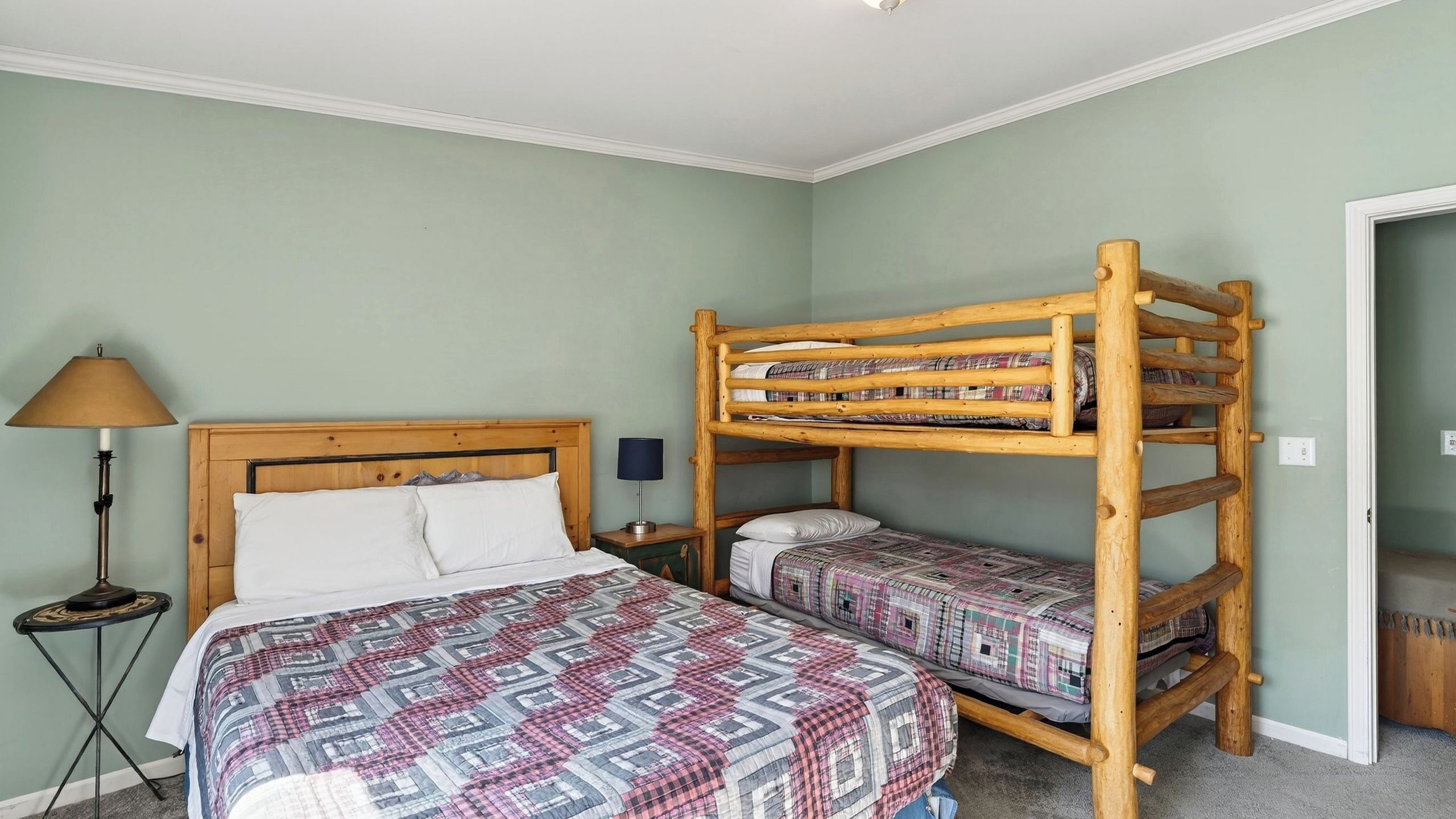A bunk bed with a patterned bedspread, a bedside table with a lamp, and a wall-mounted shelf.