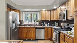 A modern kitchen with wooden cabinets, stainless steel appliances, and a window with blinds. - Gold King Lodge by Avantstay Hot Tub + Game Room + Fireplace Mins to Peak 9 + Historic Main Street (Breckenridge)