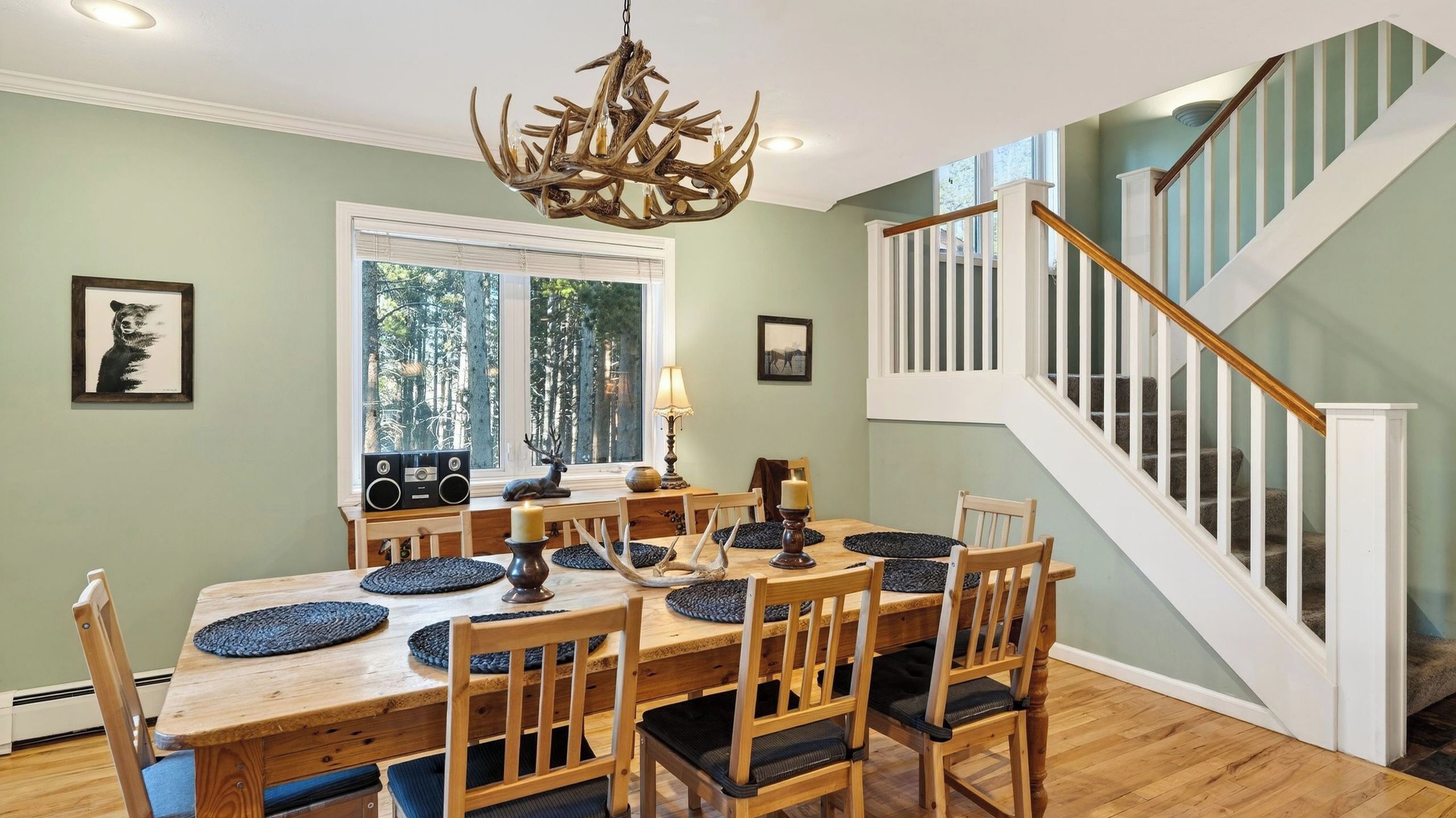 A dining area with a wooden table and chairs, a chandelier, and a staircase.