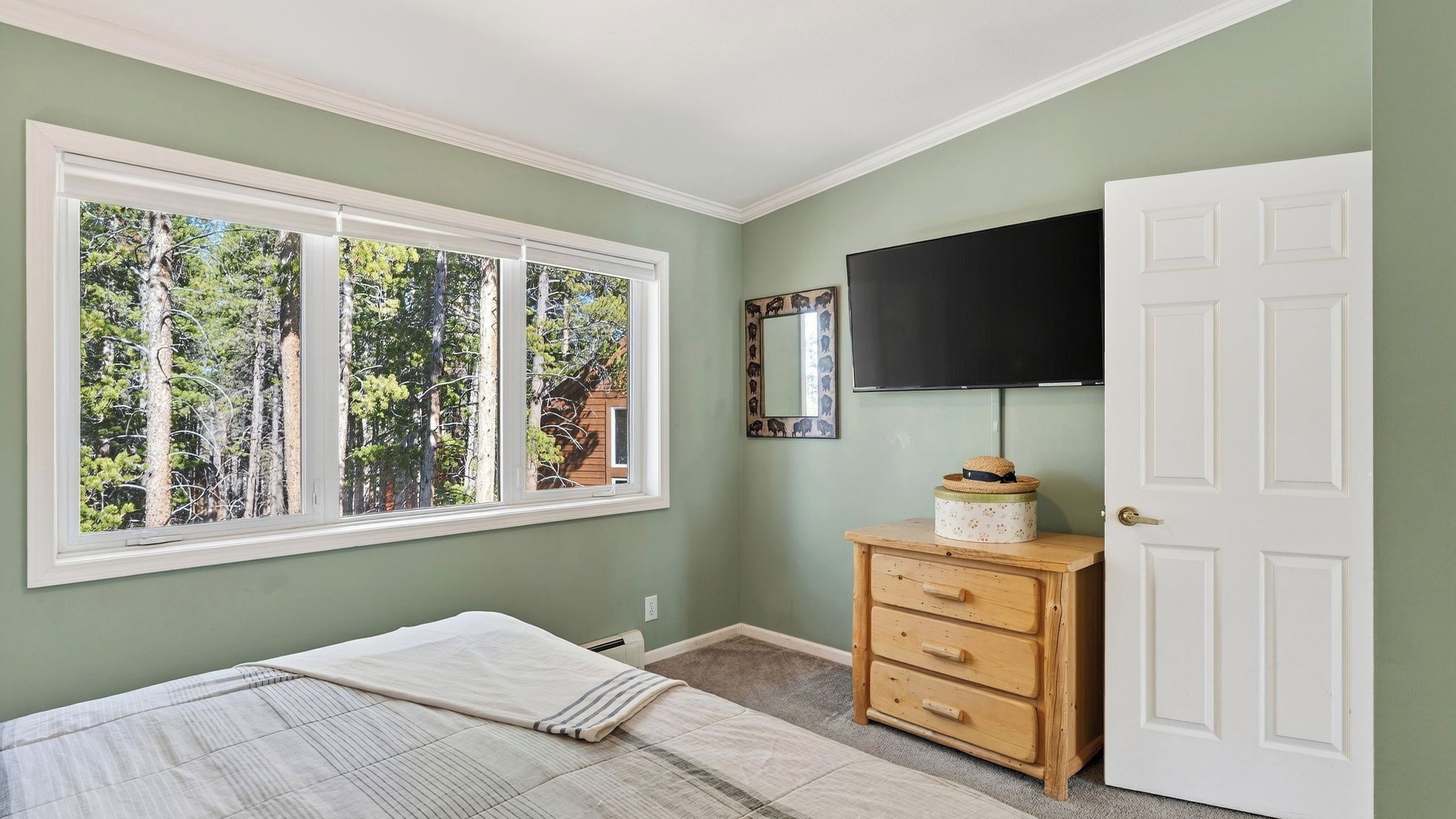 A bedroom with a large window, a bed, a dresser, and a television.