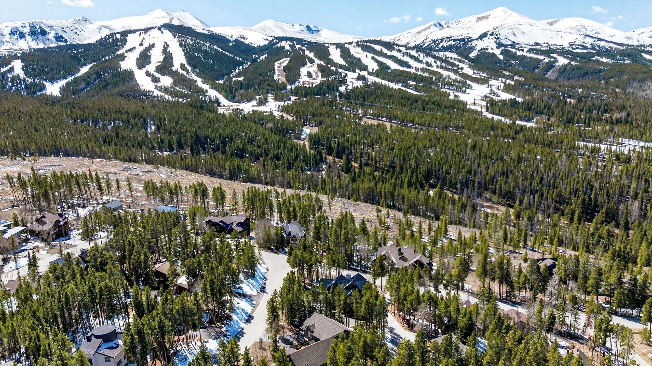 A mountainous area with snow-covered peaks, dense forests, and several buildings with distinct roofs.