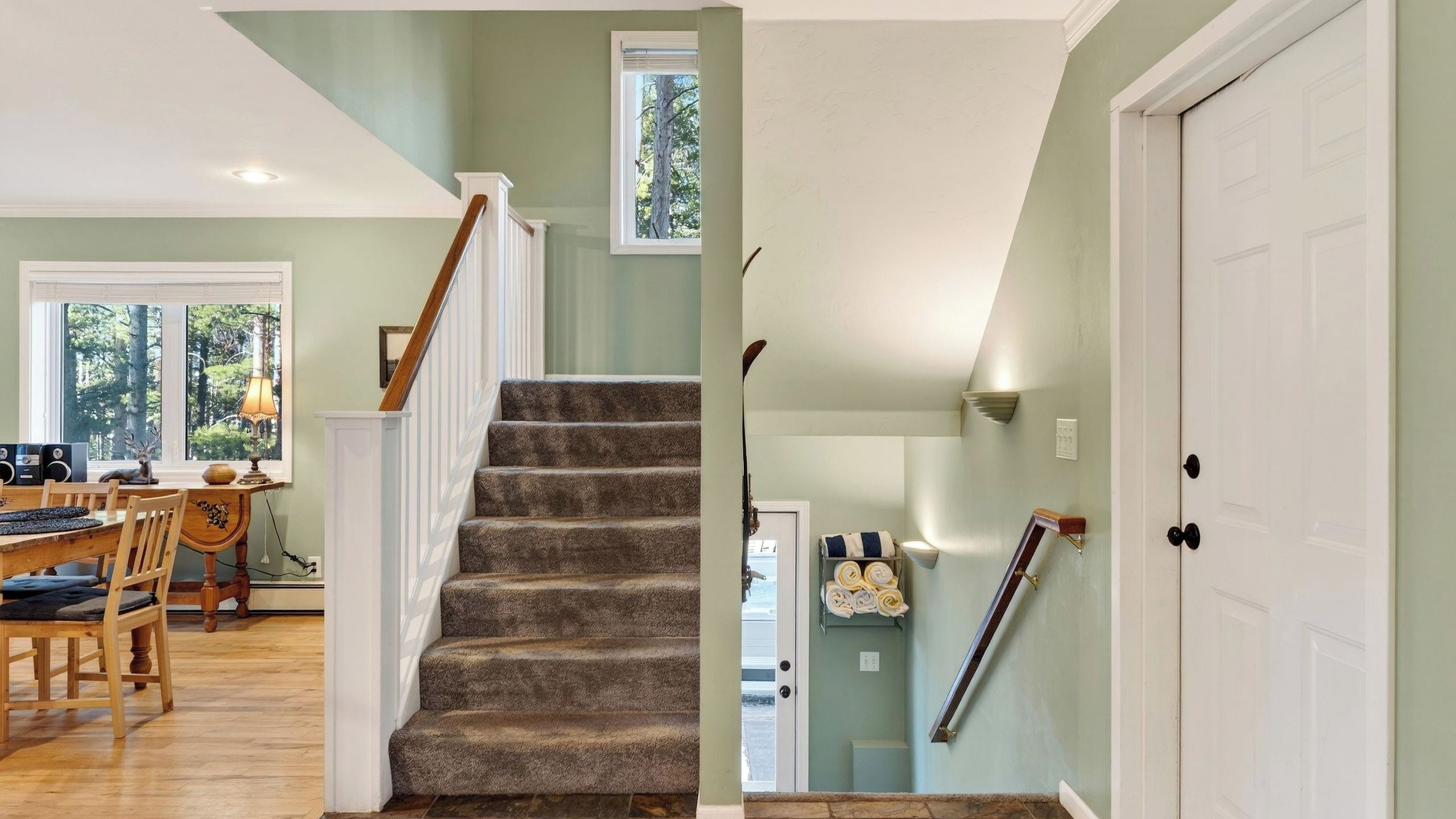 A staircase with carpeted steps, a dining area with a table and chairs, and a door with a towel rack.