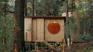 A wooden cabin with a circular window, surrounded by forest.