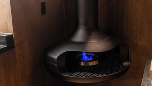 A modern kitchen with a built-in wood-burning stove, wooden cabinetry, and a granite countertop.