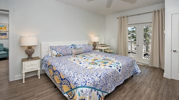 Une chambre à coucher avec un lit, des tables de chevet, un ventilateur de plafond et une vue sur l’extérieur.