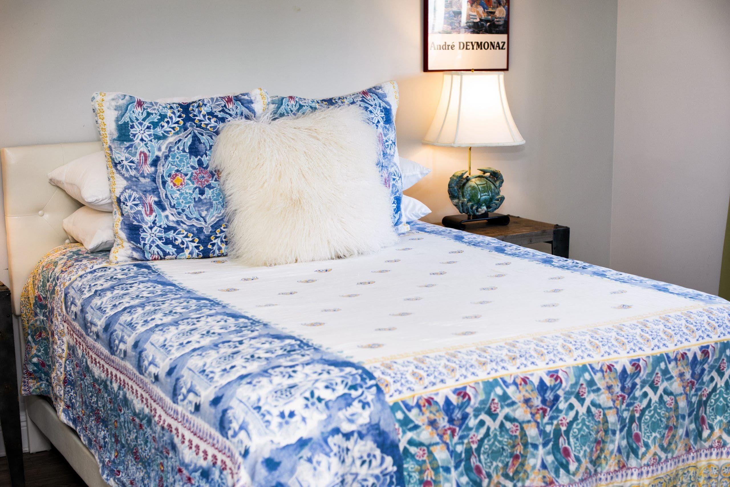 Una cama con una colcha estampada, un almohadón mullido y un cuadro en la pared.