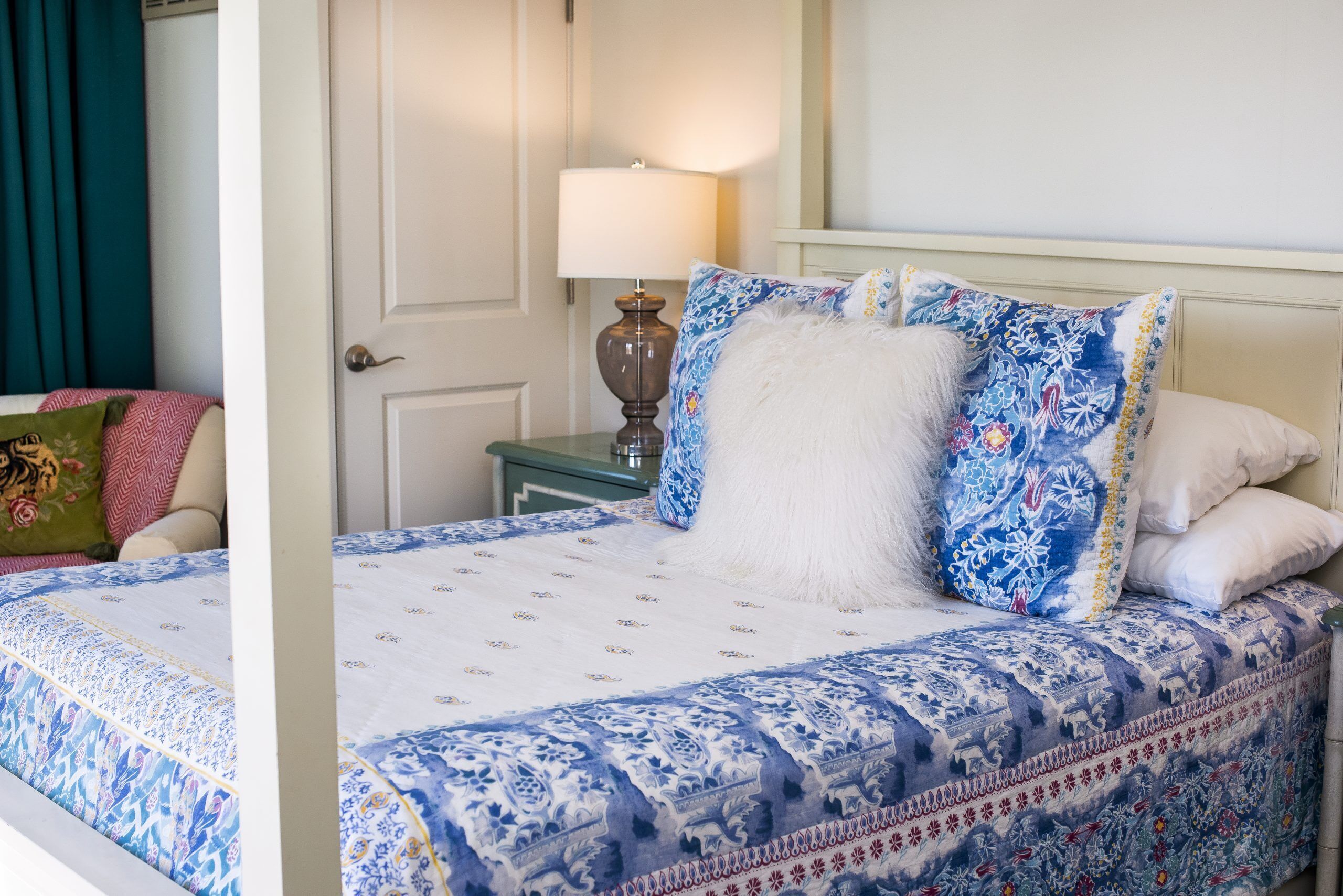 A bed with a patterned bedspread, a bedside lamp, and a door in the background.