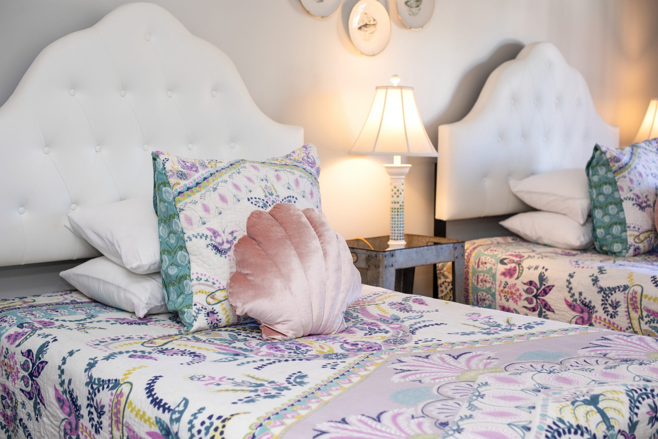 Un dormitorio con cabecera capitonada, ropa de cama con estampado floral y una lámpara de noche.