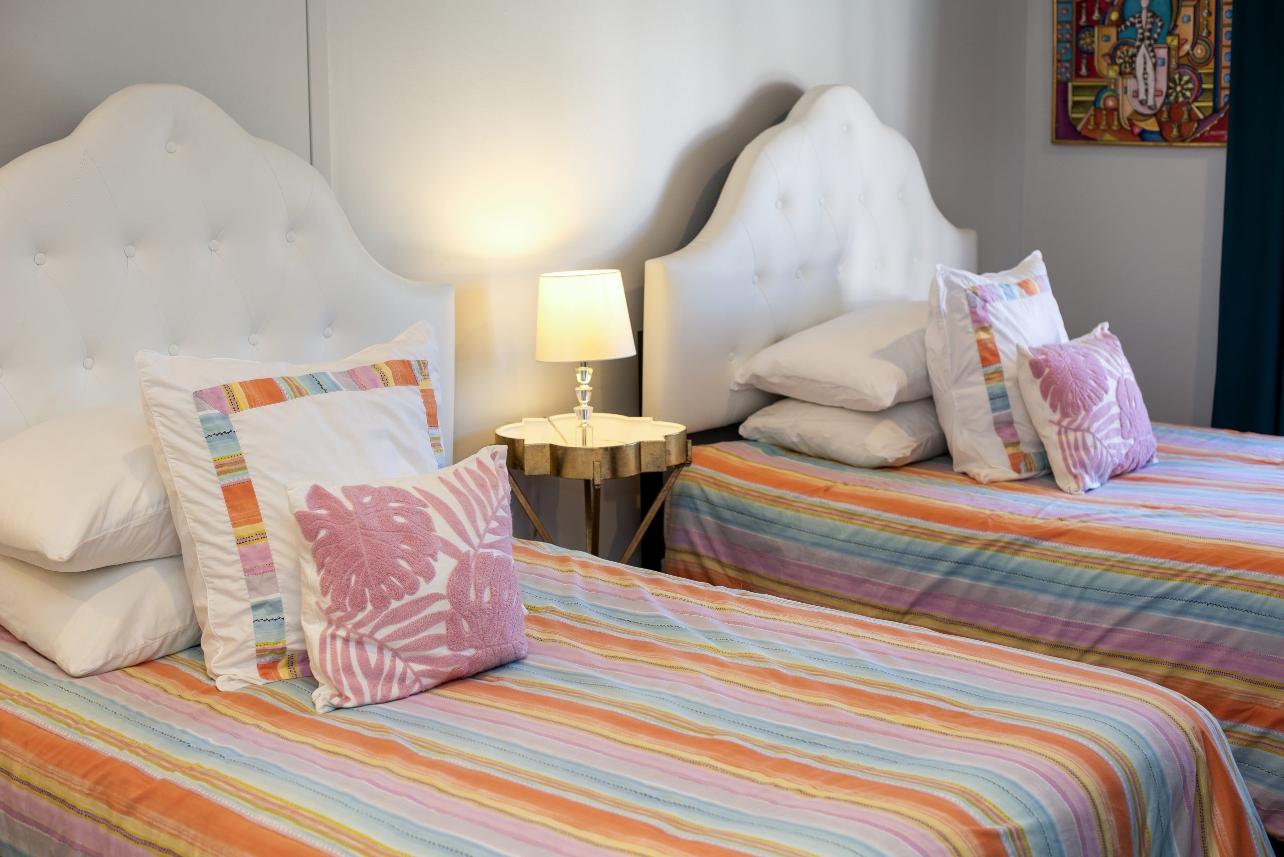 Une chambre d’hôtel avec deux lits, chacun agrémenté de draps à rayures et de coussins décoratifs. Une petite table ronde avec une lampe se trouve entre les deux lits.