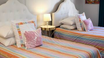 Habitación de hotel con dos camas, cada una con ropa de cama a rayas y almohadas decorativas. Hay una pequeña mesa redonda con una lámpara entre las camas.
