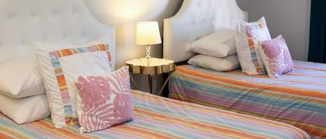 Une chambre d’hôtel avec deux lits, chacun agrémenté de draps à rayures et de coussins décoratifs. Une petite table ronde avec une lampe se trouve entre les deux lits.