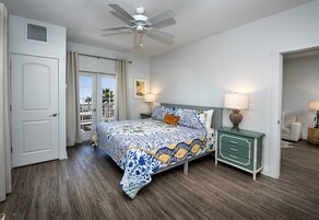 Un dormitorio con cama, mesita de noche, ventilador de techo, puerta y vistas al exterior.