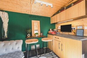 A compact kitchen with a green wall, wooden cabinets, a TV, and two bar stools.