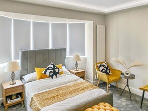 A modern bedroom with a large bed, bedside tables, a chair, and a small table with a lamp.
