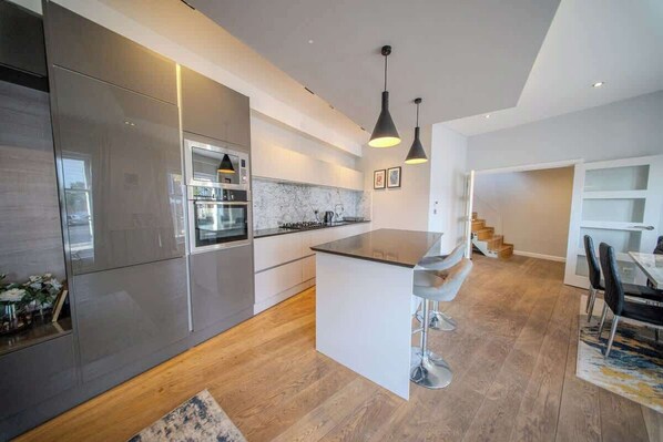 A modern kitchen with stainless steel appliances, a marble backsplash, and a central island with bar stools.
