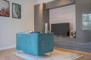 A modern living room with a teal sofa, a flat-screen TV, and abstract art on the wall.