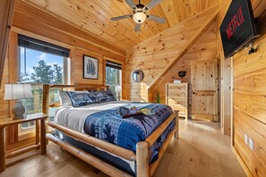 Ein Schlafzimmer einer Holzhütte mit einem Bett, einem Deckenventilator, einem Fernseher und einem Fenster.