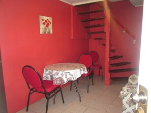 A dining area with a table and chairs, a staircase, and a wall with a floral painting.