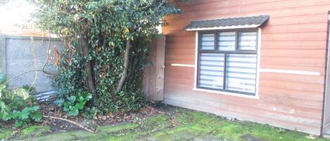 Una casa de madera con ventana y un árbol en primer plano.