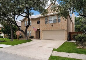 A two-story house with a garage, a front lawn, and a flag. - Sleeps 20 w/Pool Near SeaWorld/6-flags & AFB (San Antonio)