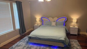 A bedroom with a bed, two bedside tables, a wall-mounted light fixture, and a window with blinds. - Sleeps 20 w/Pool Near SeaWorld/6-flags & AFB (San Antonio)