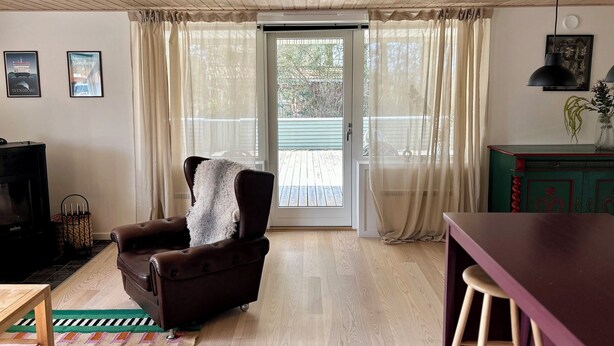 Una habitación con techo de madera, una silla de cuero marrón, una mesa de madera, un armario verde y un ventanal corredero que da a un espacio exterior.