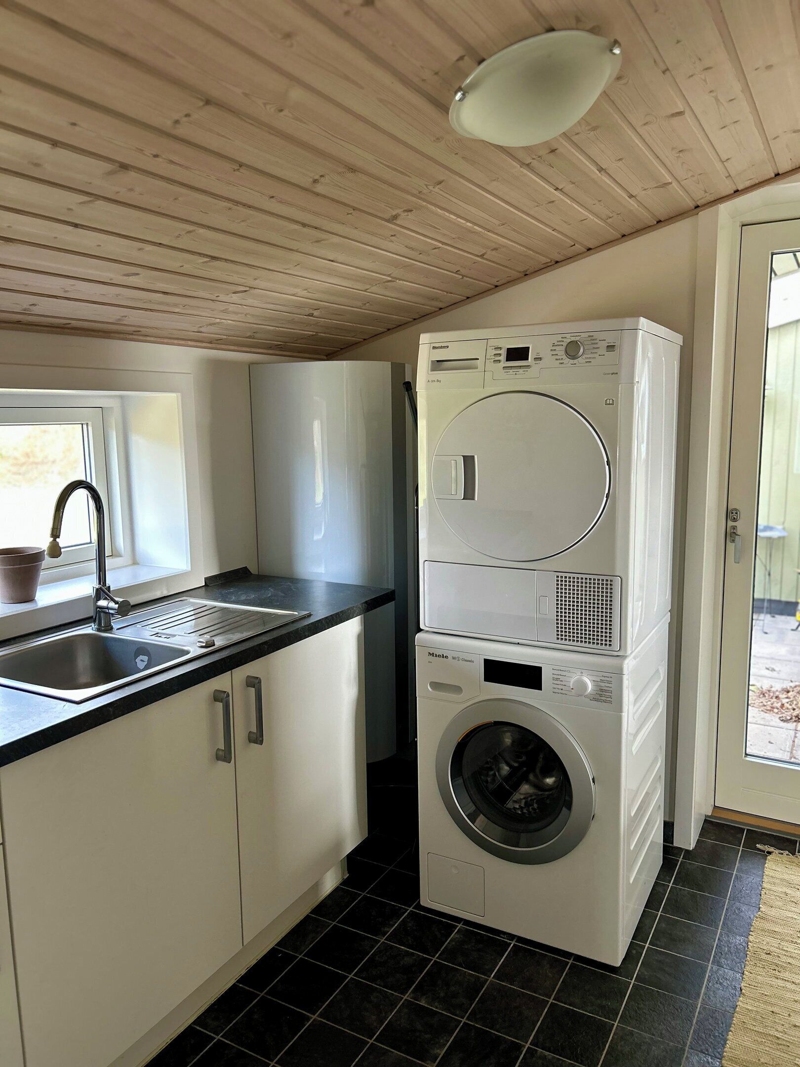 A compact kitchen with a sink, cabinets, and a stacked washer and dryer.