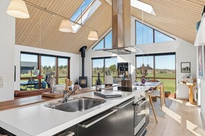 A modern kitchen with a large island, stainless steel appliances, and a view of the outdoors. - Lovely cottage next to Dejbjerg Golf Club (Skjern)