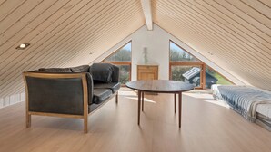 Ein Zimmer mit hohen Decken und einem geneigten Holzbalken, ein Sofa, ein Tisch und ein Bett mit Blick ins Freie.