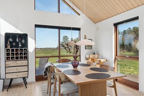 A dining area with a wooden table, chairs, and a wine rack with bottles. - Lovely cottage next to Dejbjerg Golf Club (Skjern)