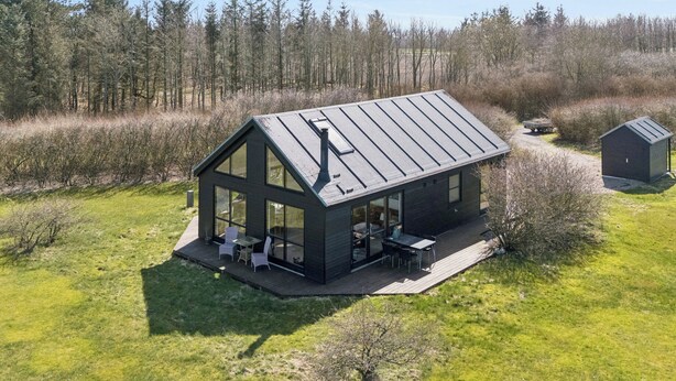Ein modernes Haus mit großer Glasfront, einer Terrasse und einem Metalldach.