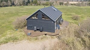 Ein modernes Haus mit Satteldach, einer Terrasse mit Sitzgelegenheiten und Blick auf ein Wiesenfeld sowie Bäume im Hintergrund.