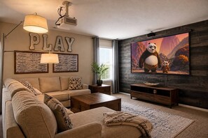 A living room with a sofa, coffee table, and a television displaying an animated film. - Fall Getaway | 5BR w/ Theater Near Randolph AFB (Converse)