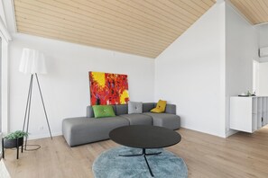 A modern living room with a grey sectional sofa, a round black coffee table, a colorful abstract painting, a white floor lamp, and a white cabinet. - New 2026 holiday home with spa near beach (Augustenborg)