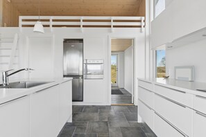 A modern kitchen with white cabinetry, a stainless steel refrigerator, and a built-in oven. - New 2026 holiday home with spa near beach (Augustenborg)