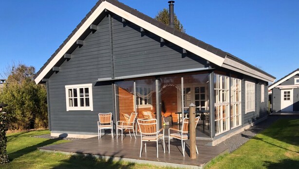 A house with a dark exterior, a large glass door, and a patio with chairs. - Cozy log cabin near beach and forest (Strøby)
