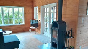 A wooden cabin interior with a fireplace, a television on a stand, and a dining area. - Cozy log cabin near beach and forest (Strøby)
