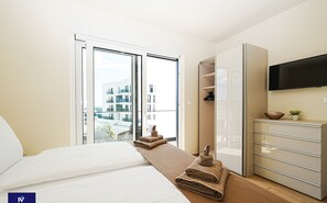 Ein Hotelzimmer mit Bett, großem Fenster, Wandfernseher und Holzkommode.