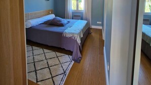 Un dormitorio con cama, ventilador de techo, ventana con cortinas y piso de madera.
