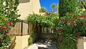 Un sendero estrecho bordeado por exuberante follaje y flores rojas, que conduce a un portón de madera.