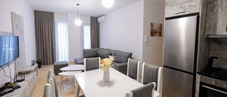 A modern kitchen with a stainless steel refrigerator, a dining table with chairs, a sofa, and a flat-screen TV.