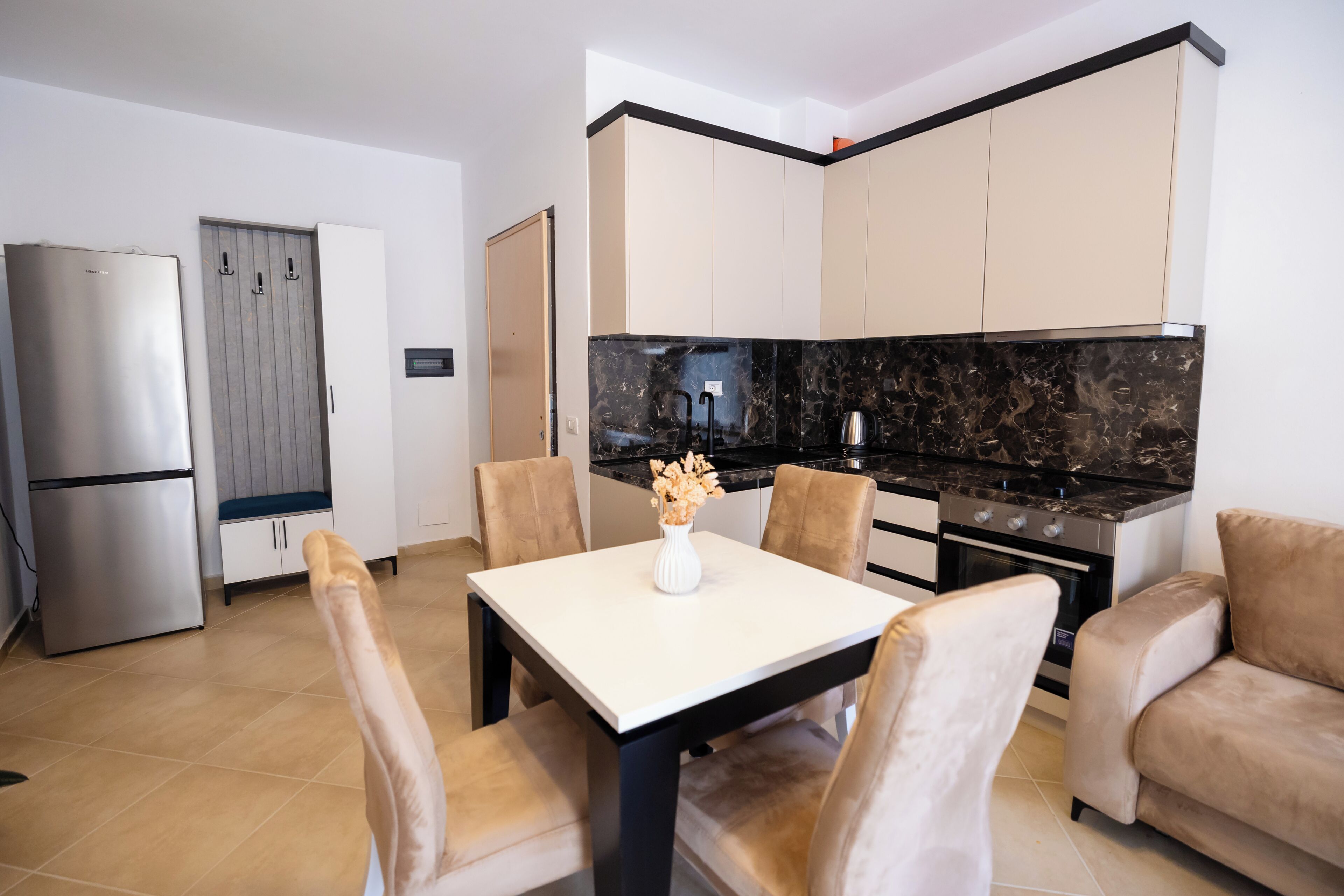 A modern kitchen with a marble countertop, a dining table with chairs, and a refrigerator.