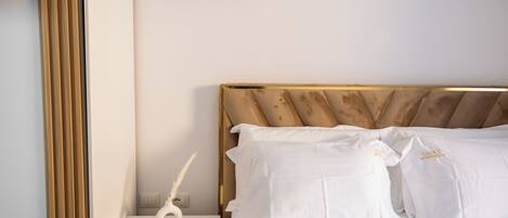 A neatly made bed with white linens and pillows, a bedside table with a white vase and a feather pen, and a wooden headboard.