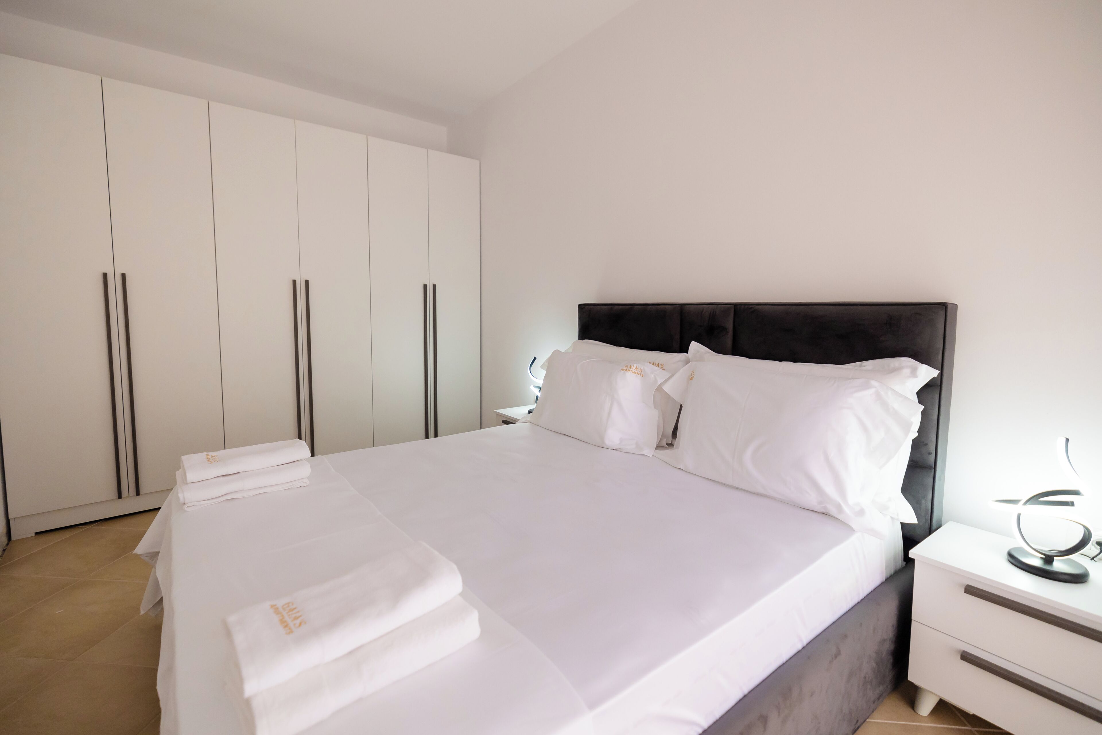 A neatly made bed with white linens, a dark headboard, and a bedside table with a lamp.