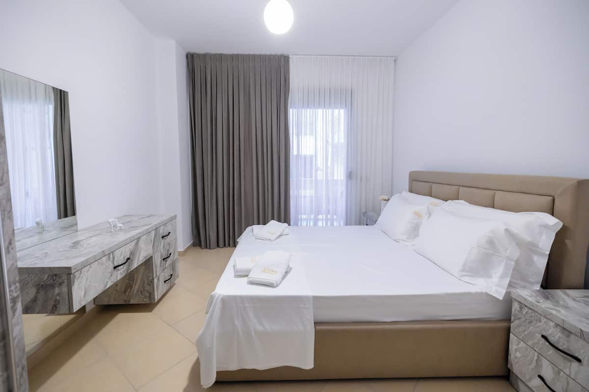 A hotel room with a bed, a marble vanity, a large mirror, and a window with curtains.