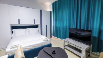 A hotel room with a bed, a flat-screen TV on a wooden stand, a small table, and a blue accent wall.
