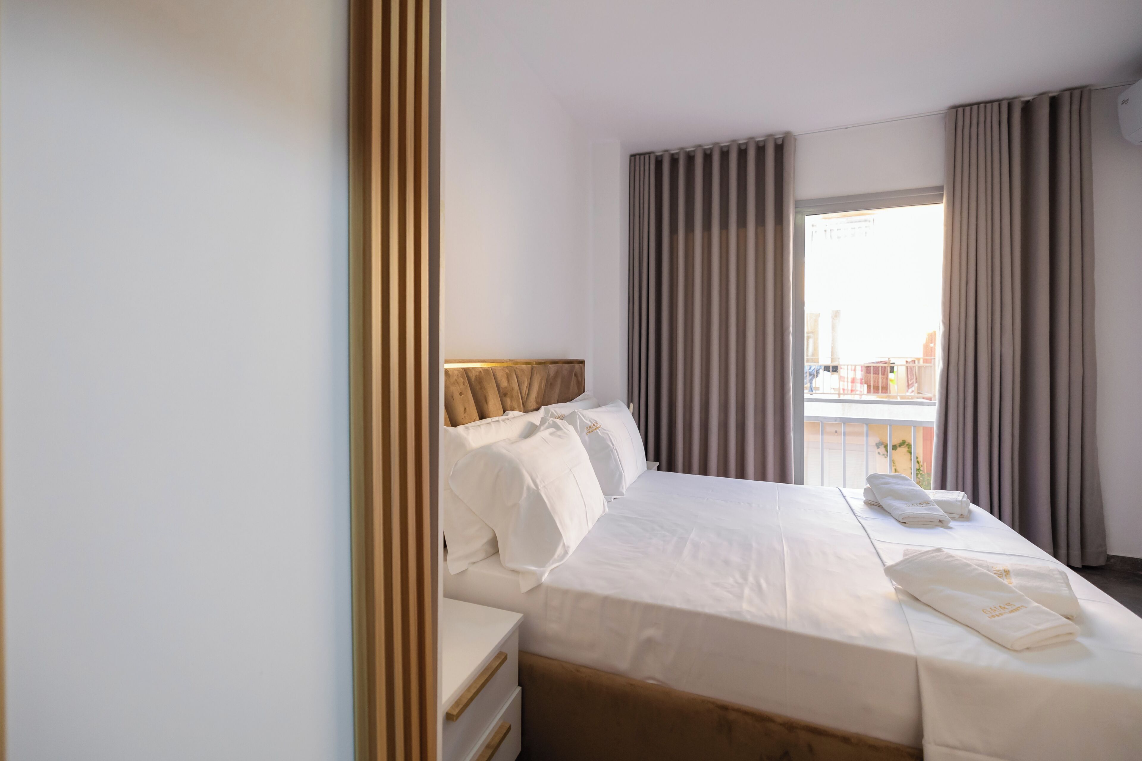 Ein Hotelzimmer mit Bett, Nachttisch, einem Fenster mit Vorhängen und Blick nach draußen.